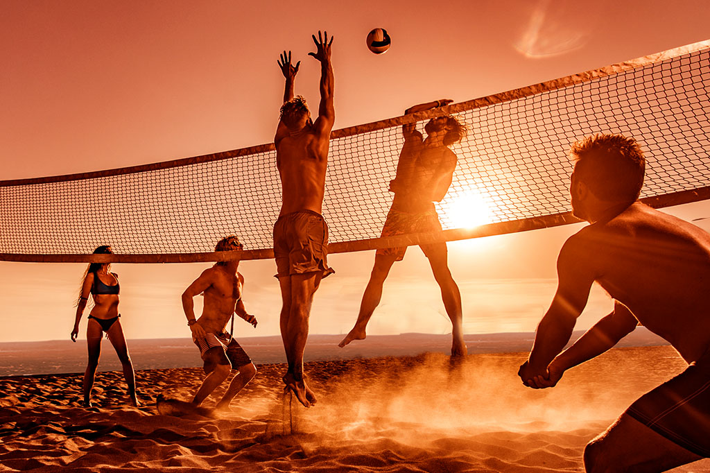 Young friends having fun while playing beach volleyball at sunset.